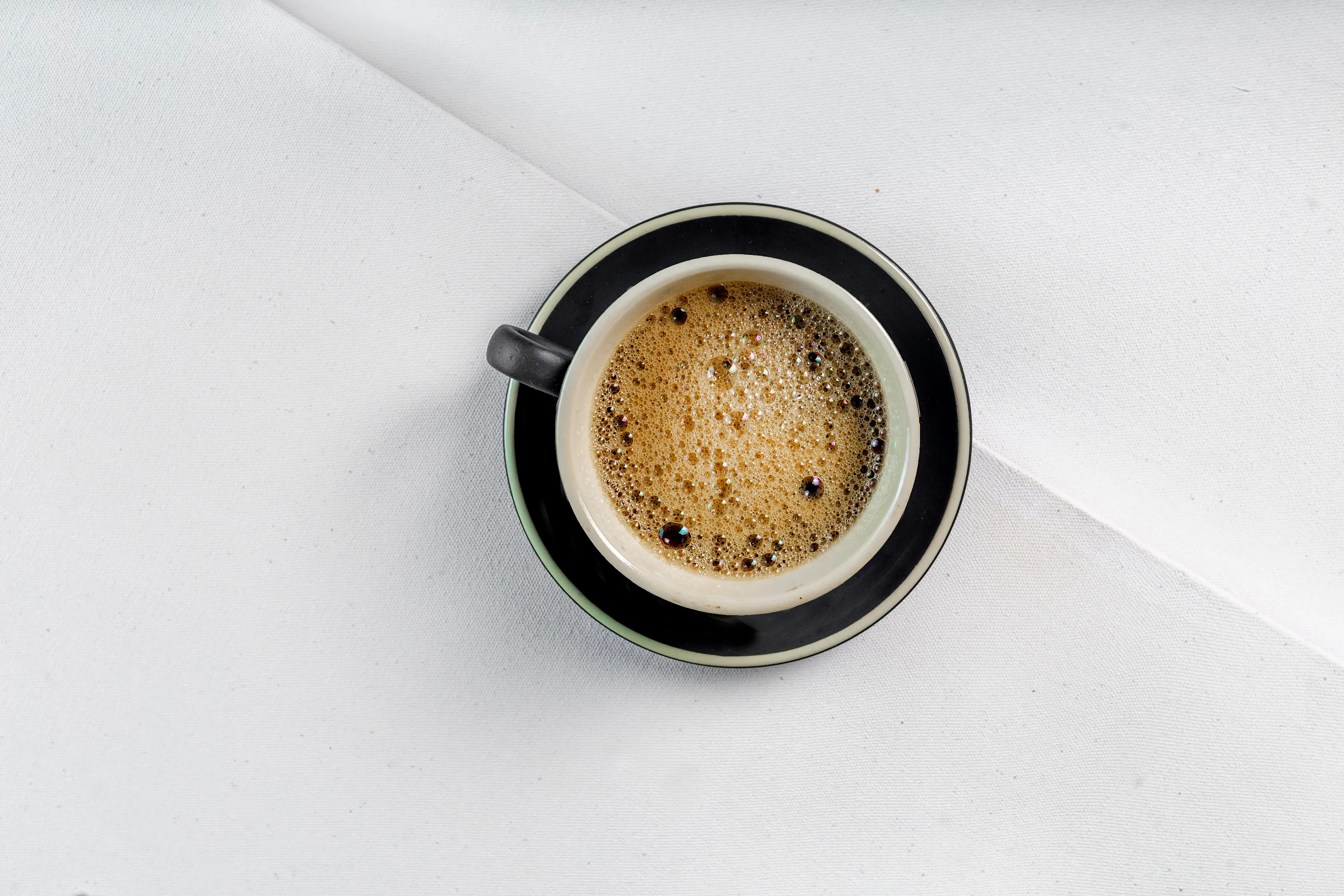 Uma xícara de café expresso vista de cima, sozinha sobre uma superfície branca.